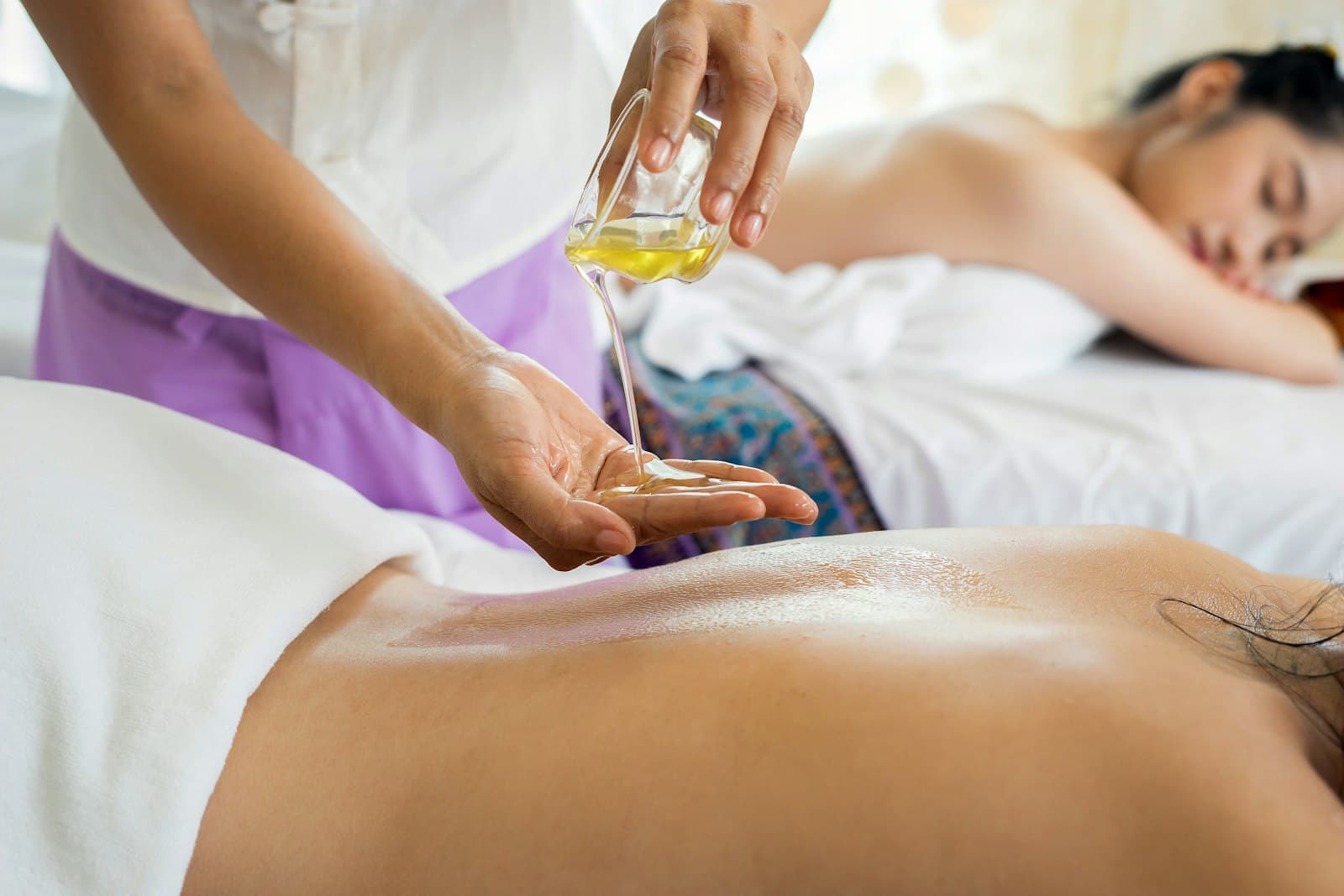 Massage oil being poured into a hand beside a person's back
